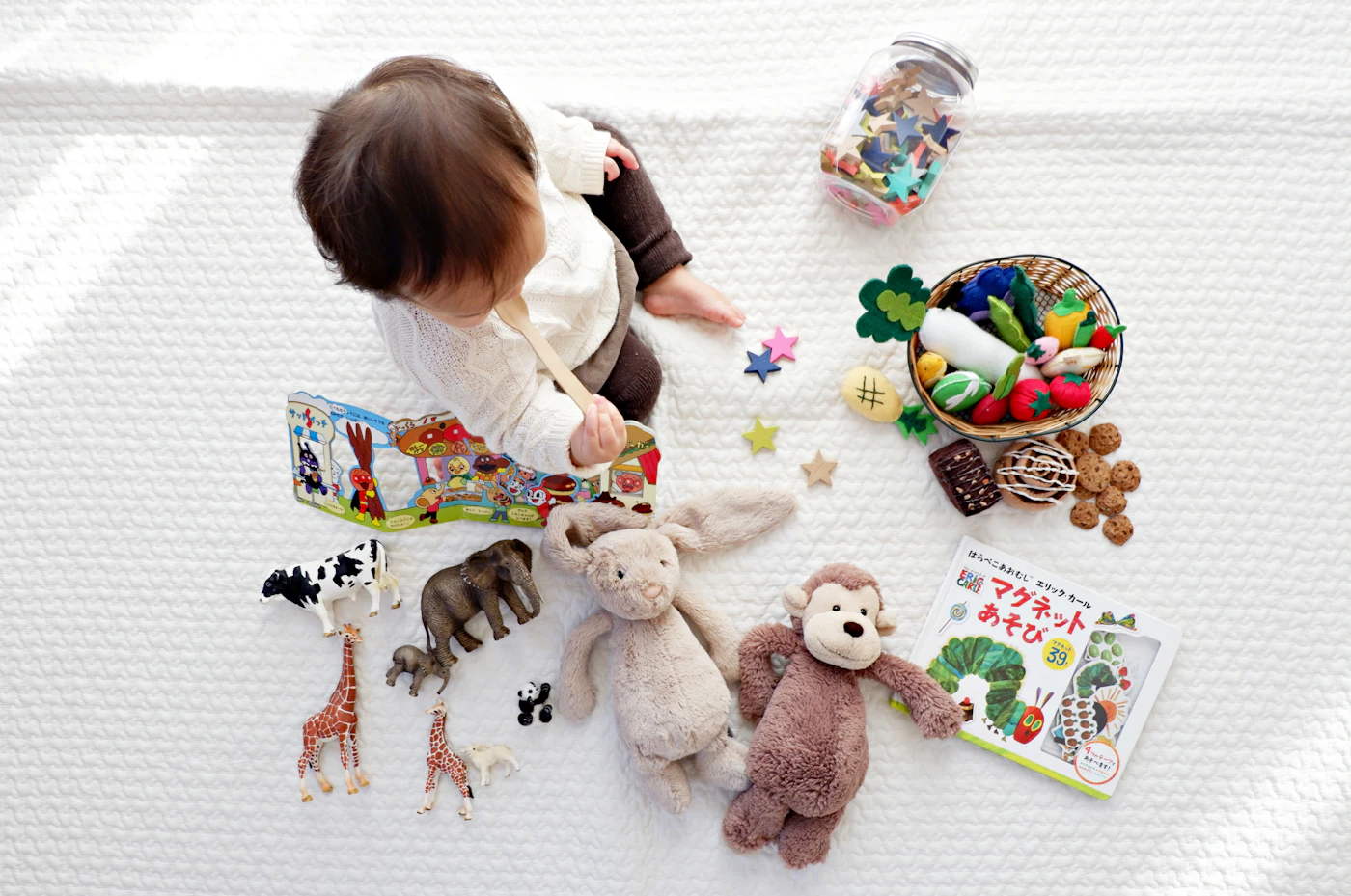 Un bébé assis au milieu de peluches, de livres et de jouets