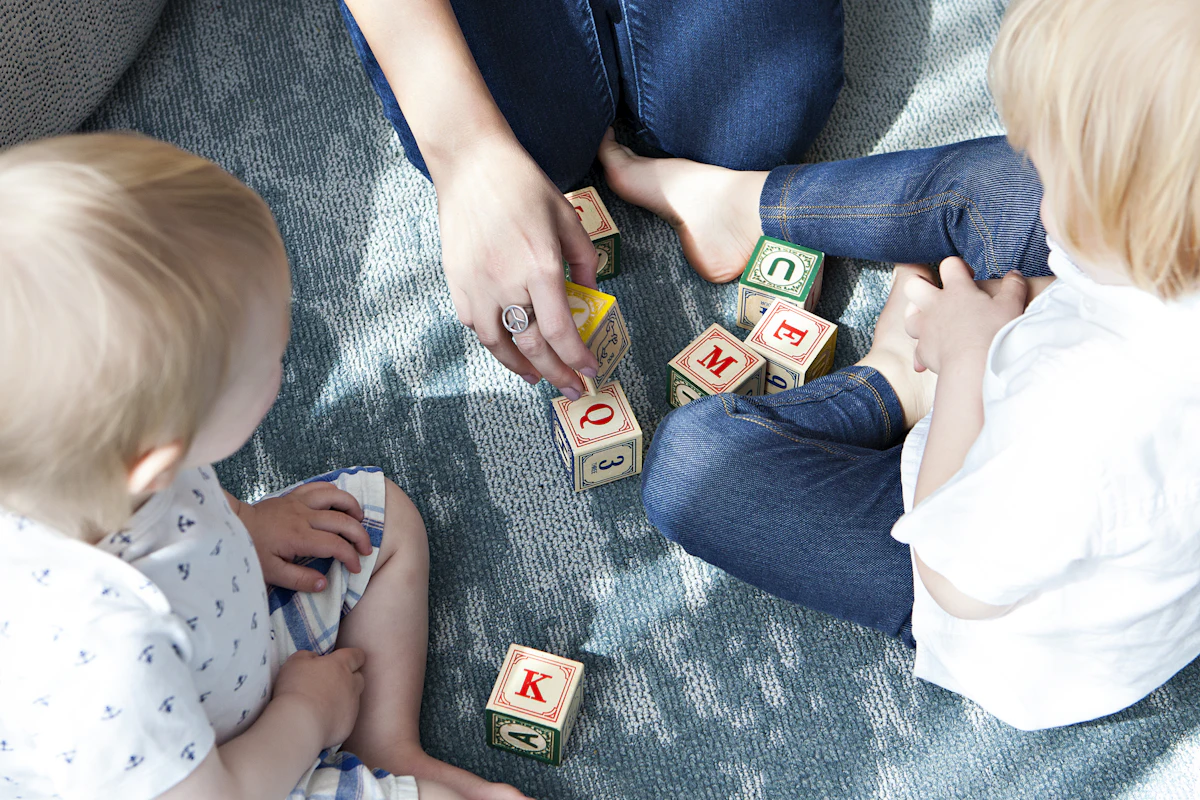 Des adultes assis par terre jouent aux cubes à lettres avec deux tout-petits