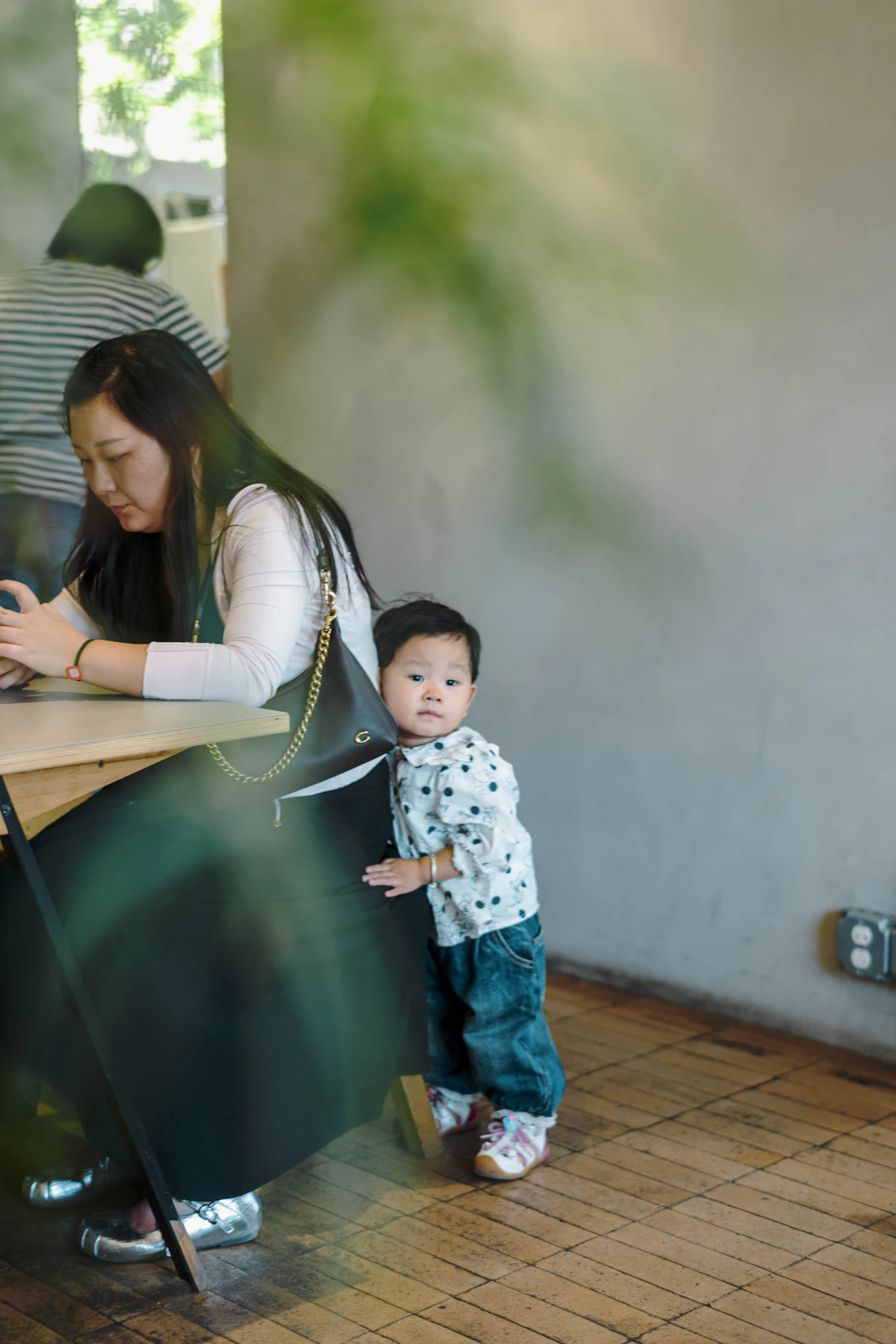 Une femme travaille à une table, une petite fille appuyée contre sa chaise